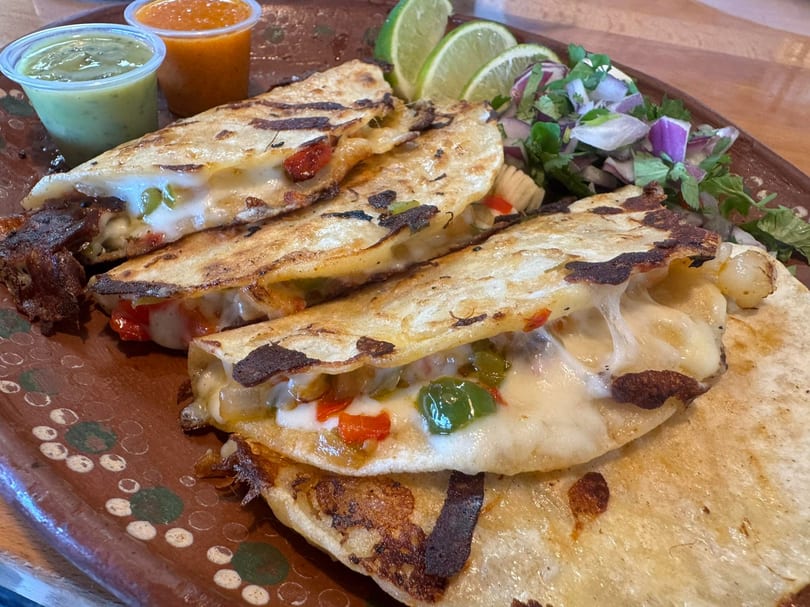 Cheesy quesadillas with green and red peppers, served with salsa, limes, and a side salad.