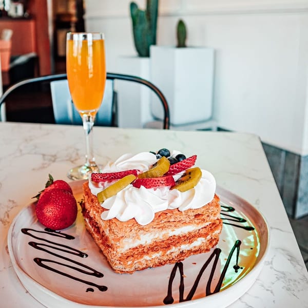 Mille-feuille pastry with whipped cream, strawberries, kiwi, and blueberries, next to a mimosa.