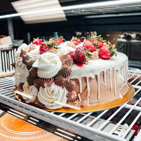 Chocolate and vanilla cake with white icing, chocolate rosettes, and fresh strawberries in a display case.
