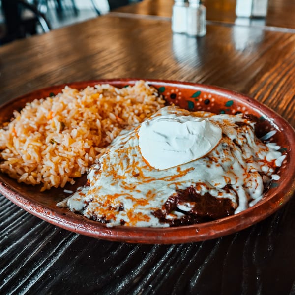 A plate of enchiladas covered in melted cheese and sour cream, served with a side of rice.