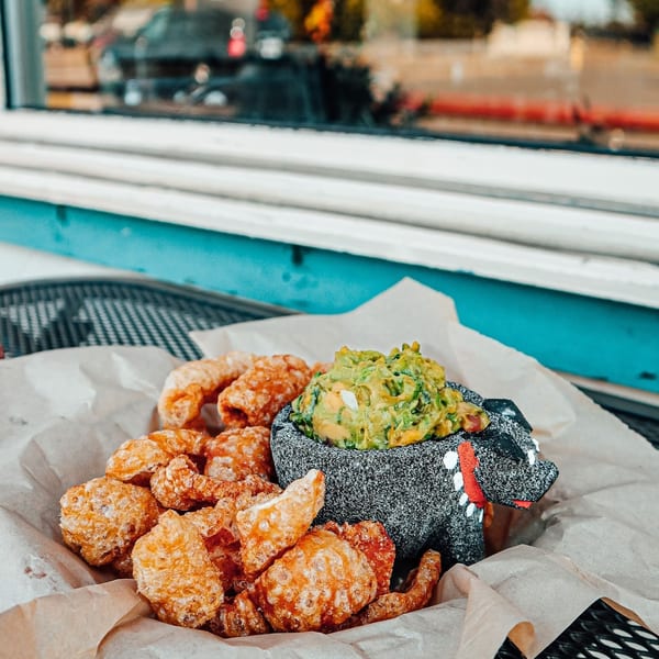 Chicharrones and guacamole in a pig-shaped molcajete on a table by a window.
