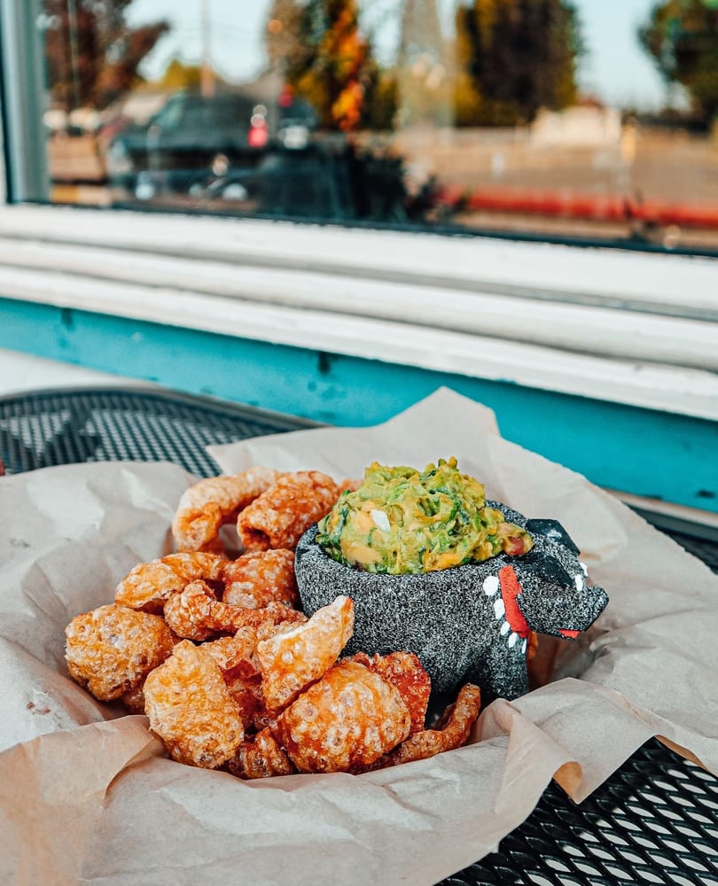 Chicharrones and guacamole in a pig-shaped molcajete on a table by a window.